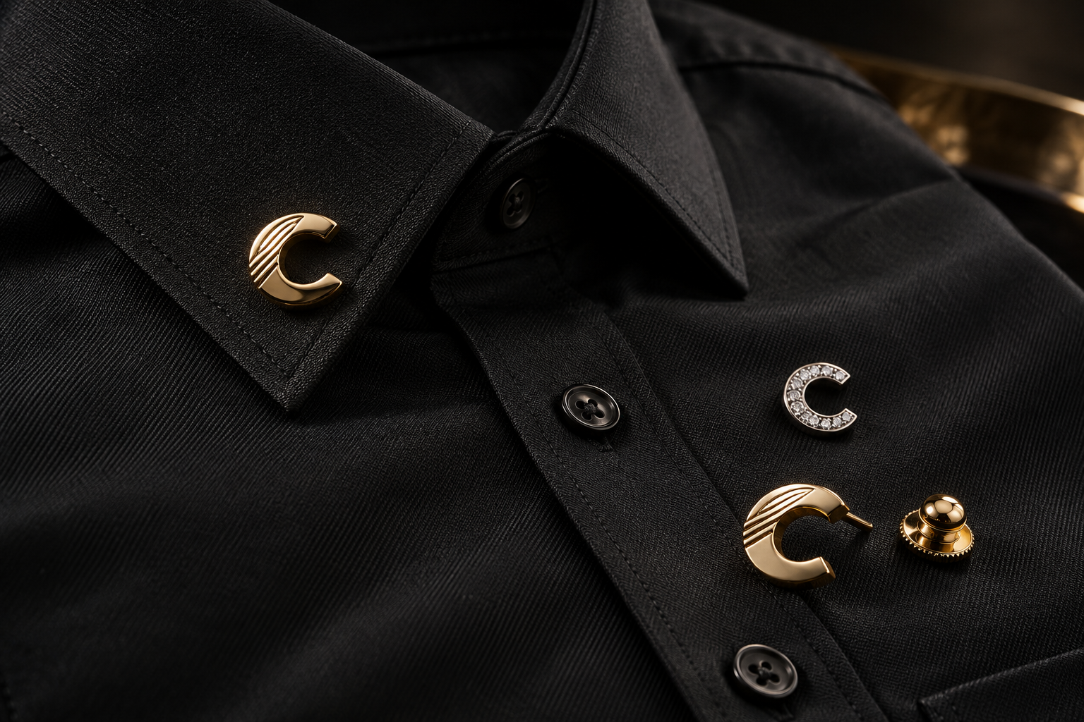 Precious-material design study of gold and silver C jewelry details with discreet diamonds on black tailored fabric.