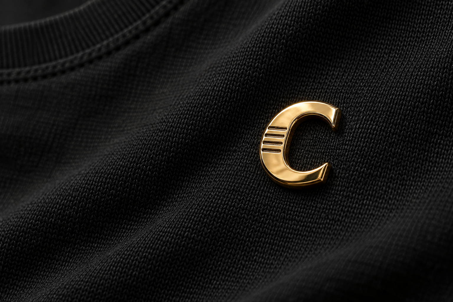 Close-up concept of a sculptural gold C with four engraved lines against black fabric.